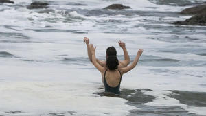 A couple react as they take a mid-winter swim at Bronte Beach as rain continues to fall in Sydney, Australia, Wednesday, July 6, 2022. More than 50,000 residents of Sydney and its surrounds have been told to evacuate or prepare to abandon their homes on Tuesday as Australia's largest city braces for what could be its worst flooding in 18 months. (AP Photo/Mark Baker)