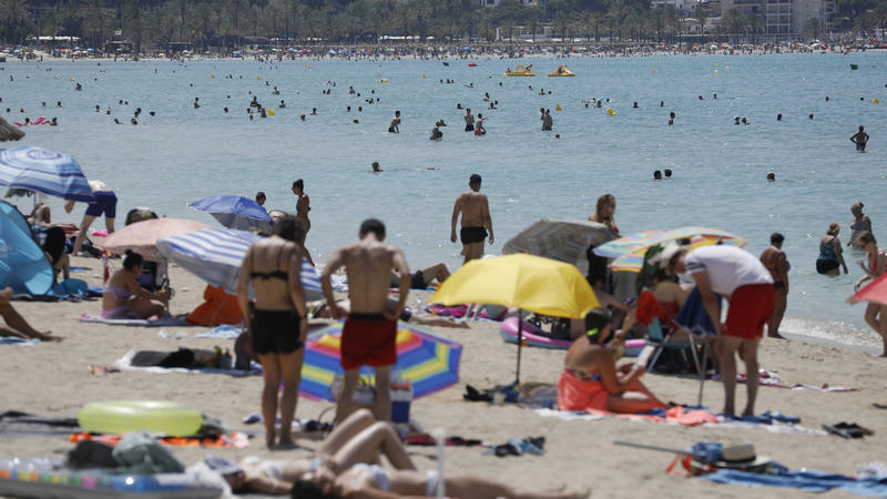 Palma: Menschen liegen am Strand von Arenal auf Mallorca in der Sonne, während andere sich im Wasser abkühlen.