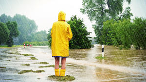 Frau steht mit Regenmantel im Starkregen - Überflutung