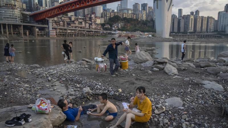 20.08.2022, China, Chongqing: Menschen sitzen in einem flachen Wasserbecken im Flussbett des Jialing-Flusses, eines Nebenflusses des Jangtse, in der südwestchinesischen Stadt Chongqing. Die Landschaft von Chongqing, einer Millionenstadt.