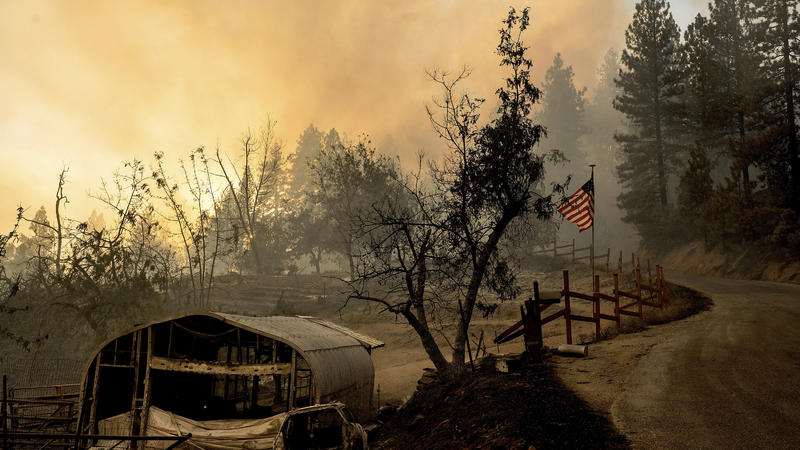 dpatopbilder - 08.09.2022, USA, Unincorporated Placer County: Eine US-fahne weht hinter einem verbrannten Nebengebäude, während der Waldbrände des sogenannten Mosquito-Feuers . Foto: Noah Berger/FR34727 AP/dpa +++ dpa-Bildfunk +++