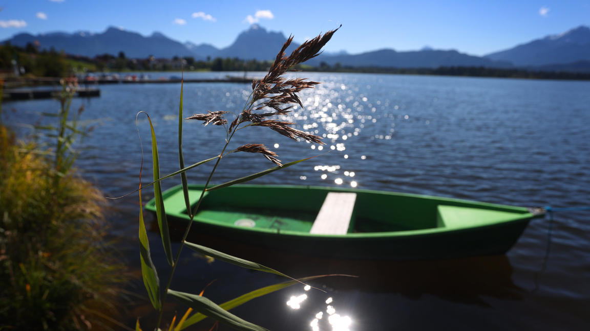 Bayern, Füssen: Ein Boot liegt an einem Steg auf dem im Sonnenschein glitzernden Hopfensee. Foto: Karl-Josef Hildenbrand/dpa +++ dpa-Bildfunk +++