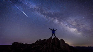 Mensch beobachtet Sternschnuppen mit Milchstraße im Hintergrund