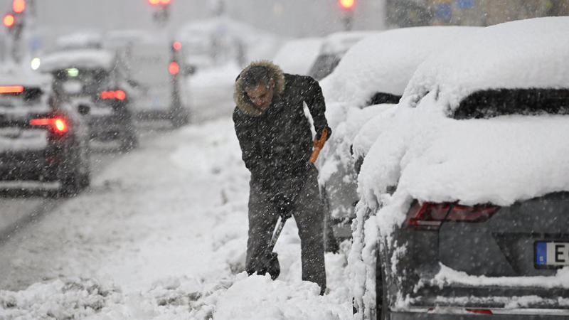 Stockholm: Ein Mann schaufelt Schnee weg, um sein Auto von einem Parkplatz während eines starken Schneefalls zu befreien