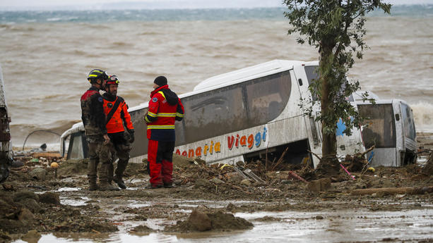 Rescuers stand next to a bus carried away after heavy rainfall triggered landslides that collapsed buildings and left as many as 12 people missing, in Casamicciola, on the southern Italian island of Ischia, Saturday, Nov. 26, 2022. Firefighters are working on rescue efforts as reinforcements are being sent from nearby Naples, but are encountering difficulties in reaching the island either by motorboat or helicopter due to the weather. (AP Photo/Salvatore Laporta)