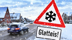 Gefahrenschild mit Aufschrift Glatteis vor verschneiter Straße