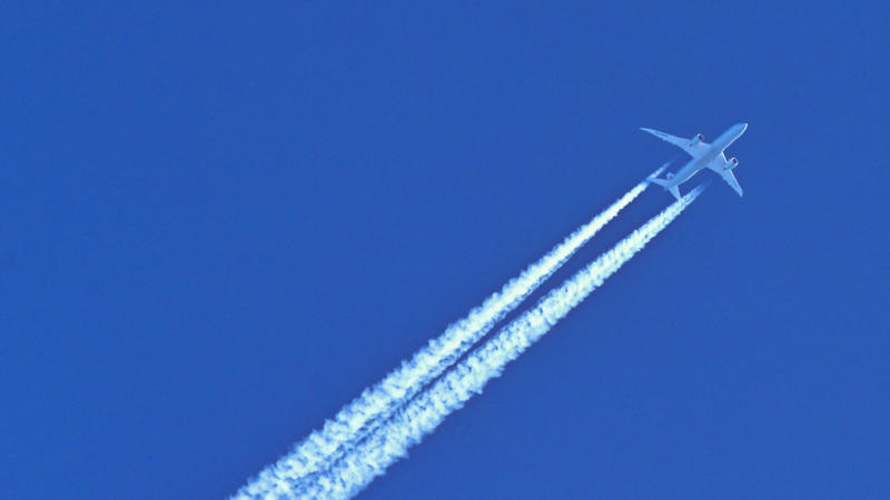 Am blauen Himmel fliegt ein Flugzeug und hinterlässt Kondensstreifen. 