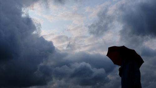 ARCHIV - 12.07.2019, Nordrhein-Westfalen, Duisburg: Ein Mann geht mit einem Regenschirm vor aufziehenden dunklen Wolken spazieren. Das Wetter war im Winter 2022/23 zu warm, und es fiel ungewöhnlich viel Regen. Das teilte der DWD am Montag mit (zu: «Winter in NRW zu warm»). Foto: Martin Gerten/dpa +++ dpa-Bildfunk +++