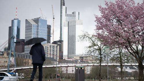 30.03.2023, Hessen, Frankfurt/Main: Ein Mann geht vor der Skyline der Innenstadt mit einem Regenschirm spazieren. Foto: Sebastian Gollnow/dpa +++ dpa-Bildfunk +++
