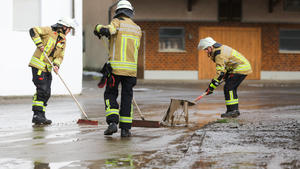 07.05.2023, Baden-Württemberg, Betzenweiler: Einsatzkräfte der Feuerwehr reinigen mit Schaufel und Besen eine vom Starkregen überflutete und verschmutzte Straße in Hailtingen. Foto: Thomas Warnack/dpa +++ dpa-Bildfunk +++