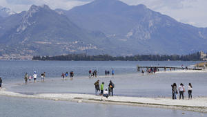 ARCHIV - 14.04.2023, Italien, Manerba del Garda: ACHTUNG: DIESER BEITRAG DARF NICHT VOR DER SPERRFRIST, 18. Mai, 20 UHR, VERÖFFENTLICHT WERDEN! EIN BRUCH DES EMBARGOS KÖNNTE DIE BERICHTERSTATTUNG ÜBER STUDIEN EMPFINDLICH EINSCHRÄNKEN. Touristen gehen über einen Streifen Land zwischen dem Festland und der Insel San Biagio, am Gardasee. Anhaltende Trockenheit und Wasserknappheit machten Italien im April weiter zu schaffen. Der Gardasee litt unter extrem niedrigen Wasserständen. (Zu dpa "Studie: Über die Hälfte der weltweit größten Seen verliert Wasser") Foto: Luca Bruno/AP/dpa +++ dpa-Bildfunk +++
