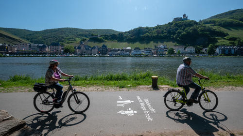29.05.2023, Rheinland-Pfalz, Bernkastel-Kues: Radfahrer radeln bei schönstem Wetter an der Mosel und Bernkastel-Kues vorbei. Auf dem Berg thront die Burg Landshut. Foto: Harald Tittel/dpa +++ dpa-Bildfunk +++