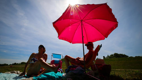 31.05.2023, Hamburg: Unter einem pinkfarbenen Sonnenschirm genießen zwei Menschen den sonnigen Tag auf einer Wiese am Elbdeich bei Ochsenwerder. Zur Mitte der Woche bleibt das Wetter im Norden des Landes sonnig und trocken. Foto: Christian Charisius/dpa +++ dpa-Bildfunk +++