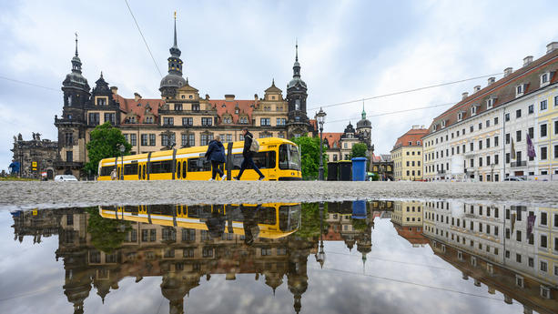 06.06.2023, Sachsen, Dresden: Eine Straßenbahn der Dresdner Verkehrsbetriebe (DVB) fährt in der Altstadt vor dem Residenzschloss entlang und spiegelt sich in einer Pfütze. Foto: Robert Michael/dpa +++ dpa-Bildfunk +++
