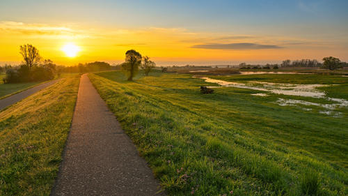 24.04.2023, Brandenburg, Lebus: Der Sonnenaufgang scheint über dem Oder-Neiße-Radweg am Deich nahe dem deutsch-polnischen Grenzfluss Oder. Foto: Patrick Pleul/dpa +++ dpa-Bildfunk +++