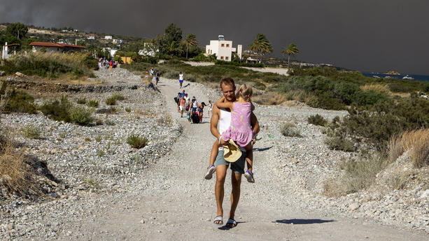 22.07.2023, Griechenland, Rhodos: Ein Mann trägt ein Kind, als sie ein Gebiet verlassen, in dem ein Waldbrand auf der griechischen Insel Rhodos wütet. Ein großes Waldfeuer, das auf der griechischen Insel Rhodos bereits den fünften Tag brennt, hat die Behörden gezwungen, die Evakuierung von vier Orten anzuordnen, darunter zwei Badeorte. Foto: Lefteris Damianidis/InTime News/AP/dpa +++ dpa-Bildfunk +++