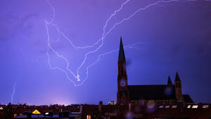 13.08.2023, Bayern, München: Ein Gewitter zieht in den Abendstunden mit Blitzen über die Dächer der bayerischen Landeshauptstadt und der St. Johann Baptist-Kirche. Foto: Peter Kneffel/dpa +++ dpa-Bildfunk +++