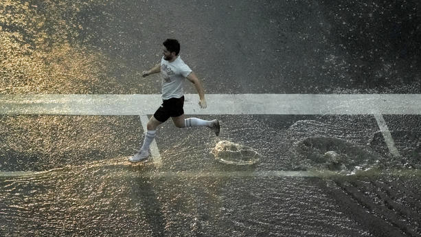 14.07.2023, USA, Kansas City: Ein Fußgänger überquert eine Straße im Regen, während ein schweres Gewitter über die Innenstadt von Kansas City zieht. Foto: Charlie Riedel/AP/dpa +++ dpa-Bildfunk +++