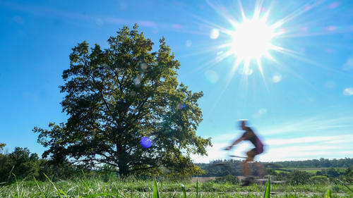 04.09.2023, Baden-Württemberg, Stuttgart: Bei strahlendem Sonnenschein und blauem Himmel fährt ein Radfahrer durch einen Park bei Stuttgart (Wischeffekt durch Langzeitbelichtung). Foto: Bernd Weißbrod/dpa +++ dpa-Bildfunk +++