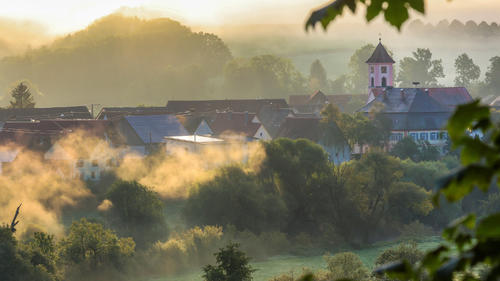 20.09.2023, Baden-Württemberg, Riedlingen: Rund um die Kirche in Zell an der Donau steigt am Morgen von der Sonne gelb gefärbter Morgennebel auf. Foto: Thomas Warnack/dpa +++ dpa-Bildfunk +++