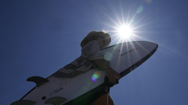 19.09.2023, Australien, Sydney: Eine Frau trägt ihr Surfbrett am Bondi Beach. In Sydney wurde zum ersten Mal seit fast drei Jahren ein absolutes Feuerverbot verhängt, und mehrere Schulen an der Südküste des Bundesstaates New South Wales wurden wegen erhöhter Waldbrandgefahr bei außergewöhnlich hohen Temperaturen im Südosten Australiens geschlossen. Inmitten einer für die Jahreszeit ungewöhnlichen Hitzewelle hat Australien offiziell das Wetterphänomen El Niño für das Land ausgerufen. Foto: Rick Rycroft/AP +++ dpa-Bildfunk +++