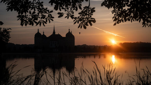 26.09.2023, Sachsen, Moritzburg: Die Sonne geht am Morgen hinter dem Schloss Moritzburg, dem einstigen Jagdschloss der Wettiner bei Dresden, auf. Foto: Robert Michael/dpa +++ dpa-Bildfunk +++