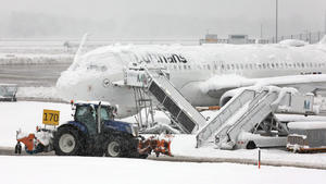 02.12.2023, Bayern, München: Ein Räum- und Streufahrzeug fährt im Schneetreiben auf dem Flughafen an einer verschneiten Maschine von Lufthansa vorbei. Die Sperrung des Flugbetriebes am Münchner Flughafen ist wegen starker Schneefälle bis 03.12.2023 um 6.00 Uhr verlängert worden. Foto: Karl-Josef Hildenbrand/dpa +++ dpa-Bildfunk +++
