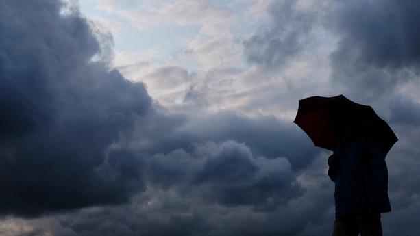 ARCHIV - 12.07.2019, Nordrhein-Westfalen, Duisburg: Ein Mann geht mit einem Regenschirm vor aufziehenden dunklen Wolken spazieren. (zu dpa: «Wolken und Regen in Nordrhein-Westfalen») Foto: Martin Gerten/dpa +++ dpa-Bildfunk +++