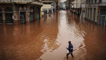 03.05.2024, Brasilien, Porto Alegre: Ein Mann watet in Porto Alegre im brasilianischen Bundesstaat Rio Grande do Sul durch ein von schweren Regenfällen überschwemmtes Gebiet. Foto: Carlos Macedo/AP/dpa +++ dpa-Bildfunk +++