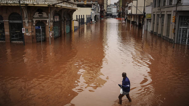 03.05.2024, Brasilien, Porto Alegre: Ein Mann watet in Porto Alegre im brasilianischen Bundesstaat Rio Grande do Sul durch ein von schweren Regenfällen überschwemmtes Gebiet. Foto: Carlos Macedo/AP/dpa +++ dpa-Bildfunk +++
