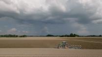 Bauer fährt mit Traktor übers Feld, während über ihm die Regenwolken stehen.