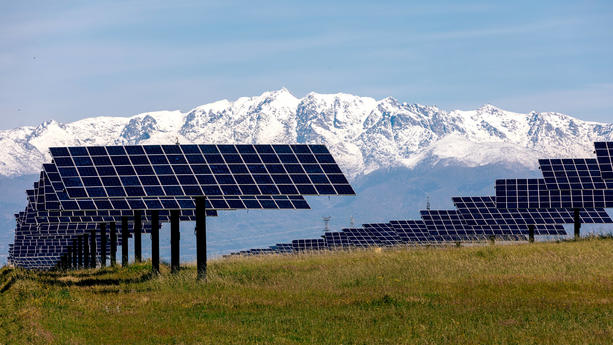 Rows of solar panels are poised in a lush field, with a stunning backdrop of snow-capped mountains under a clear blue sky. Model Released SergioVictorVega_ID21400_629664_003 Copyright: xSergioxVictorxVegax