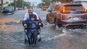 12.06.2024, USA, Miami Beach: Victor Corone, 66, schiebt seine Frau Maria Diaz, 64, in einem Rollstuhl durch Hochwasser in der 84th Street in Miami Beach. Die alljährliche Regenzeit ist in weiten Teilen Floridas mit voller Wucht angekommen, wo eine ungeordnete tropische Wetterstörung aus dem Golf von Mexiko Straßenüberschwemmungen verursacht und Tornado-Warnungen ausgelöst hat, aber bisher keine größeren Schäden oder Verletzungen verursacht hat. Foto: Al Diaz/Miami Herald/AP/dpa - ACHTUNG: Nur zur redaktionellen Verwendung und nur mit vollständiger Nennung des vorstehenden Credits +++ dpa-Bildfunk +++