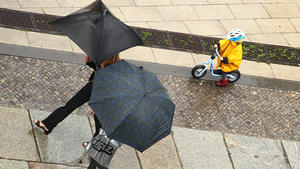 Mit Schirmen gehen zwei Erwachsene, gefolgt von einem Kind auf einem Roller in gelber Regenjacke während eines Regenschauers in Berlin-Mitte am Samstag (16.06.2012) auf einem Bürgersteig. Am Samstagvormittag gab es in der Hauptstadt starken Platzregen. Foto: Wolfram Steinberg dpa/lbn  +++(c) dpa - Bildfunk+++
