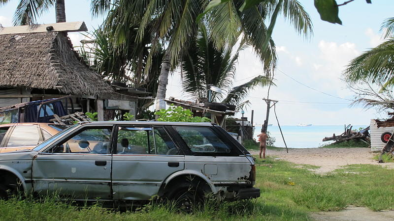 ARCHIV - Ein Autowrack steht am 25.07.2012 auf der Insel Kiribati neben ein paar Hütten. Der Inselstaat 4000 Kilometer nördlich von Neuseeland kämpft mit Überbevölkerung, Unterentwicklung und den Folgen des Klimawandels. Foto: Christiane Oelrich/dpa (zu dpa-Korr. "Familie aus Kiribati kämpft um Asyl als Klimaflüchtlinge" vom 29.10.2013) +++(c) dpa - Bildfunk+++