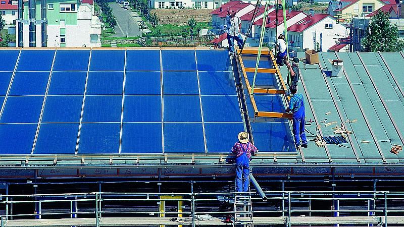 Handwerker bringen Solarzellen auf einem Hausdach an.