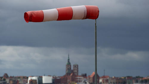 Ein Windsack steht fast horizontal in der Luft und zeigt somit recht starken Wind an, aufgenommen am 22.09.2014 in Altefähr (Mecklenburg-Vorpommern) an der Rügenbrücke auf der Insel Rügen, im Hintdergrund die Silhouette der Hansestadt Stralsund. Foto: Stefan Sauer/dpa +++(c) dpa - Bildfunk+++