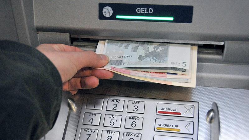 Eine Hand entnimmt dem Geldschlitz eines Bankautomaten die gewünschten Banknoten.