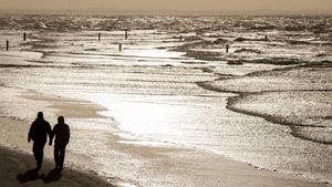 Ein Paar läuft am 02.01.2015 bei stürmischem Wetter am Strand von Norderney (Niedersachsen) vor der im Licht glitzernden Nordsee entlang. Foto: Hauke-Christian Dittrich/dpa +++(c) dpa - Bildfunk+++