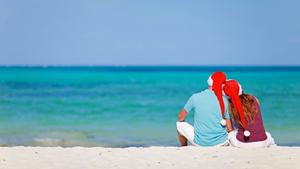 ein verliebtes Paar sitzt mit Nikolausmuetzen am Sandstrand | a couple in love sitting with Santa hats at sandy beach