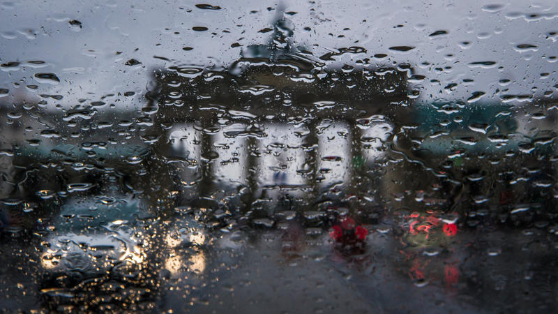 Regentropfen hängen in Berlin an einer Autoscheibe. Im Hintergrund ist das Brandenburger Tor zu erkennen.