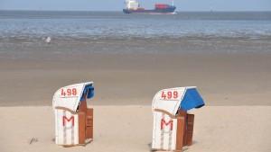 Warten auf Gäste: Während zwei Strandkörbe verschlossen am Freitag (09.04.2010) am Nordseestrand von  Cuxhaven-Döse stehen, geht ein Wanderer durchs Watt, im Hintergrund ein Containerschiff.  Foto: Carmen Jaspersen dpa/lni  +++(c) dpa - Bildfunk+++
