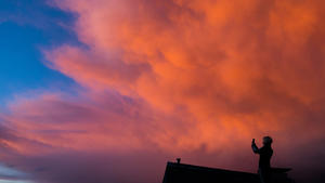 dpatopbilder Eine Frau fotografiert am 28.03.2016 in Recklinghausen (Nordrhein-Westfalen) die vom Sonnenuntergang farbig angestrahlten Gewitterwolken von einem Dach aus. Über Nordrhein-Westfalen zogen den Tag lang teils heftige Gewitter. Foto: Marcel Kusch/dpa +++(c) dpa - Bildfunk+++