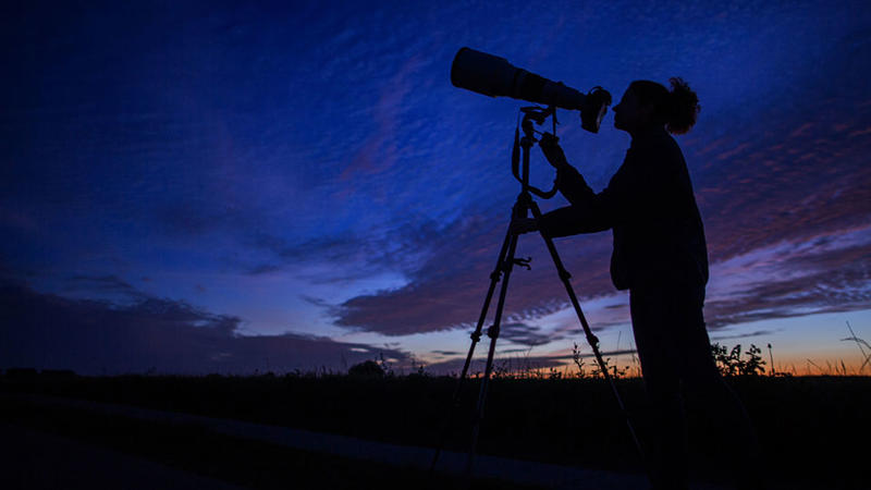 Eine Frau beobachtet durch ein Teleskop den Himmel.