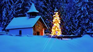 Weihnachtliche Stimmung in den Bergen. Ein erleuchteter Tannenbaum neben einer kleinen Kapelle.