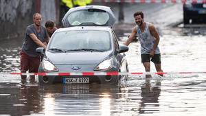 Männer schieben am 19.07.2017 ein Auto aus dem Wasser einer überfluteten Straße in Köln (Nordrhein-Westfalen). In Köln hatte es zuvor ein starkes Gewitter gegeben. Foto: Marius Becker/dpa +++(c) dpa - Bildfunk+++