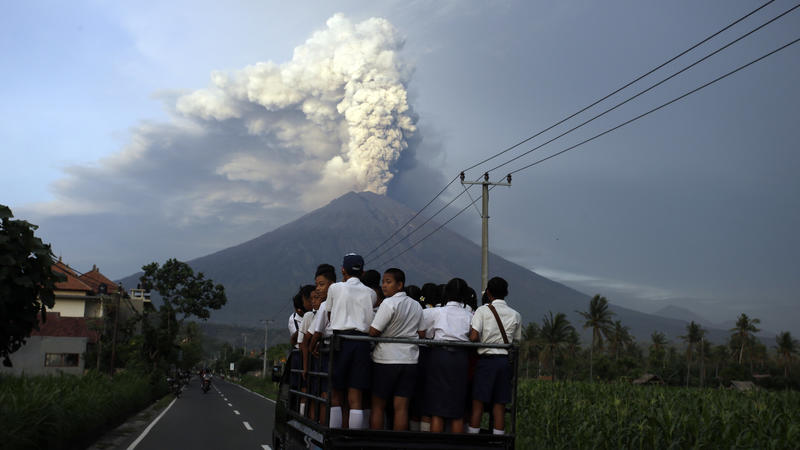 dpatopbilder - Schüler fahren am 28.11.2017 in Karangasem, Bali, Indonesien, auf ihrem Weg zur Schule auf einen Lastwagen, während der Vulkan Mount Agung im Hintergrund Rauch und Asche spuckt. Auf der indonesischen Ferieninsel Bali wird ein gewaltige